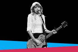 Taylor Swift sings on stage with her guitar in hand. 