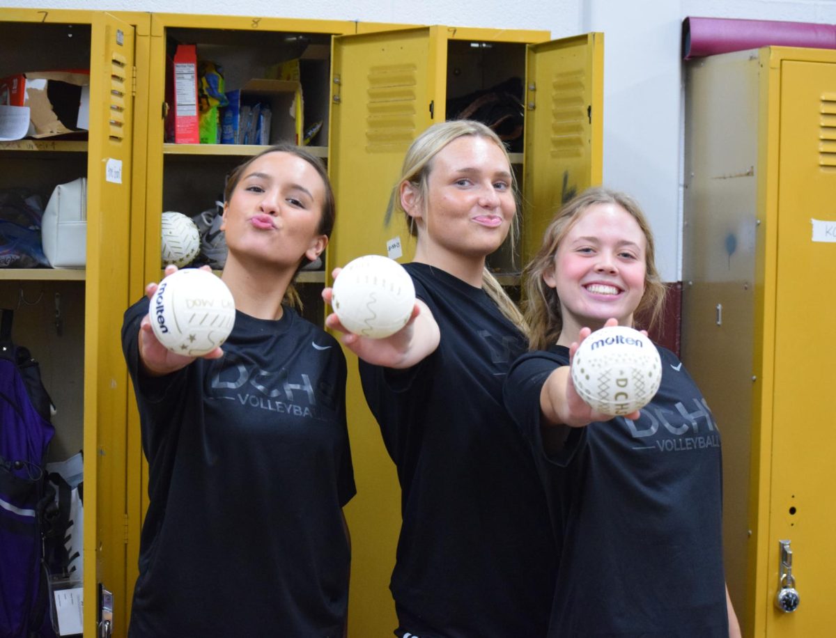 Anne Grant, Siri Beecher, and Ashley Staun hold up their decorated mini volleyballs to throw into the student section.