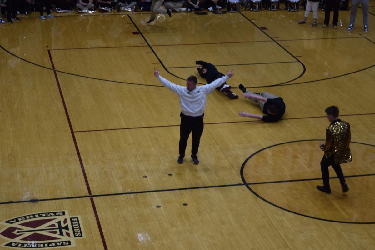 Father Flood celebrating a successful backflip after breakdancing during a pep assembly.