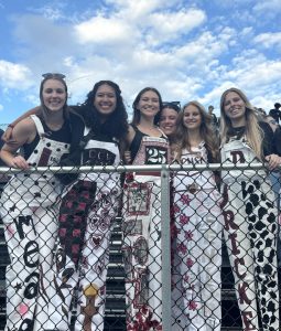 Mara Mead, Isa Colon-Alba, Elizabeth James, Franny Umstead, Lilian Schultheis, and Maddie Ricke attend a football game in their overalls.