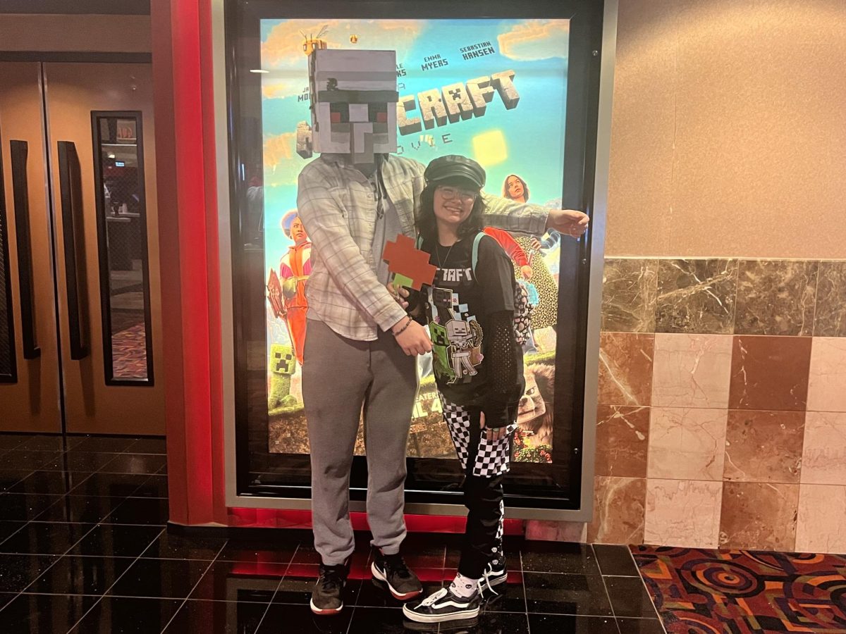 Brody Eberhart (left) and Becca Davila-Gay (right) posing in front of "A Minecraft Movie" poster