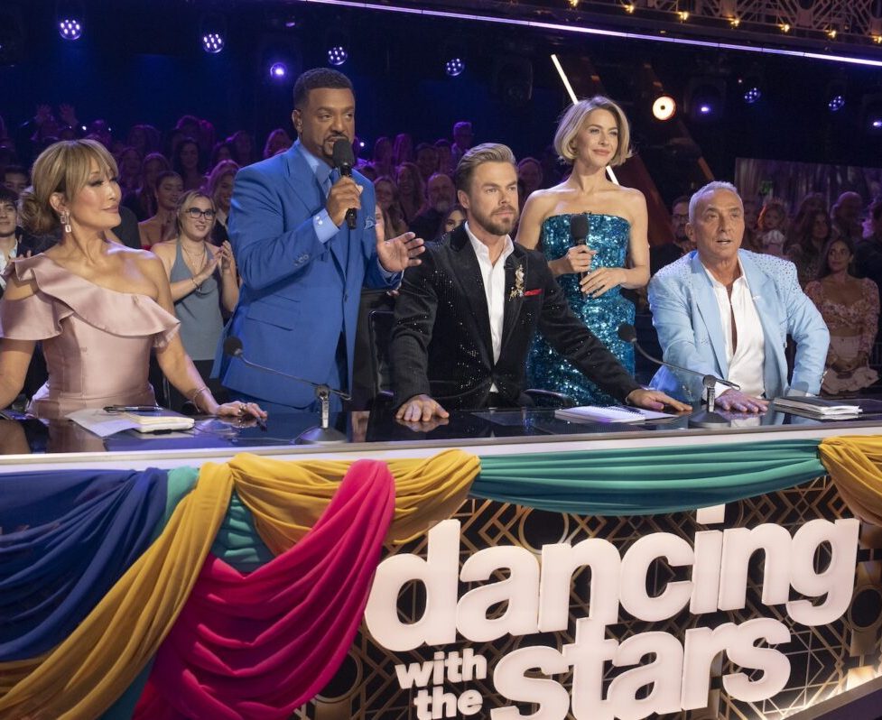 The show's hosts standing with the judges  looking at the dance floor.